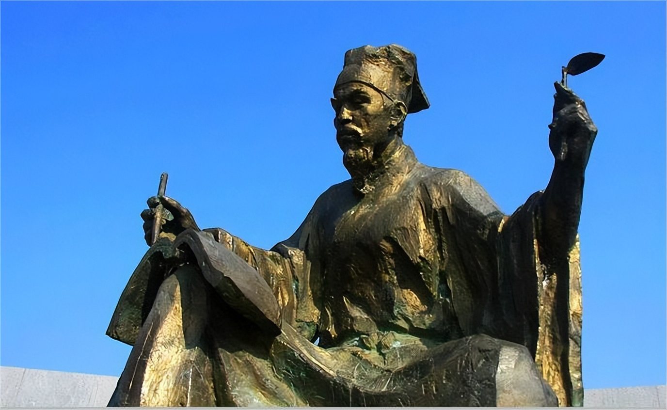 A modern bronze statue of Su Song seated, holding a brush and a leaf-shaped fan against a blue sky.